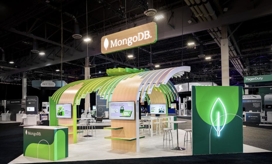 A picture of the MongoDB booth at AWS re:Invent 2021, featuring curved wooden booths and the green MongoDB leaf motif.