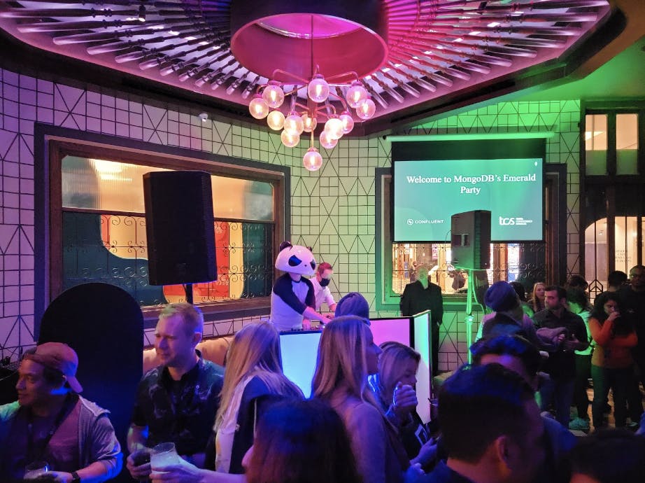 A picture of a party at Sugarcane Raw Bar Grill, with a DJ wearing a panda head and a crowd of people partying with drinks in hand.