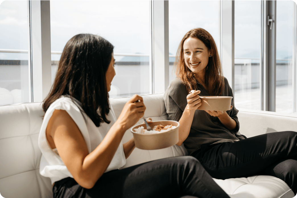 Two women eating lunch on a couch