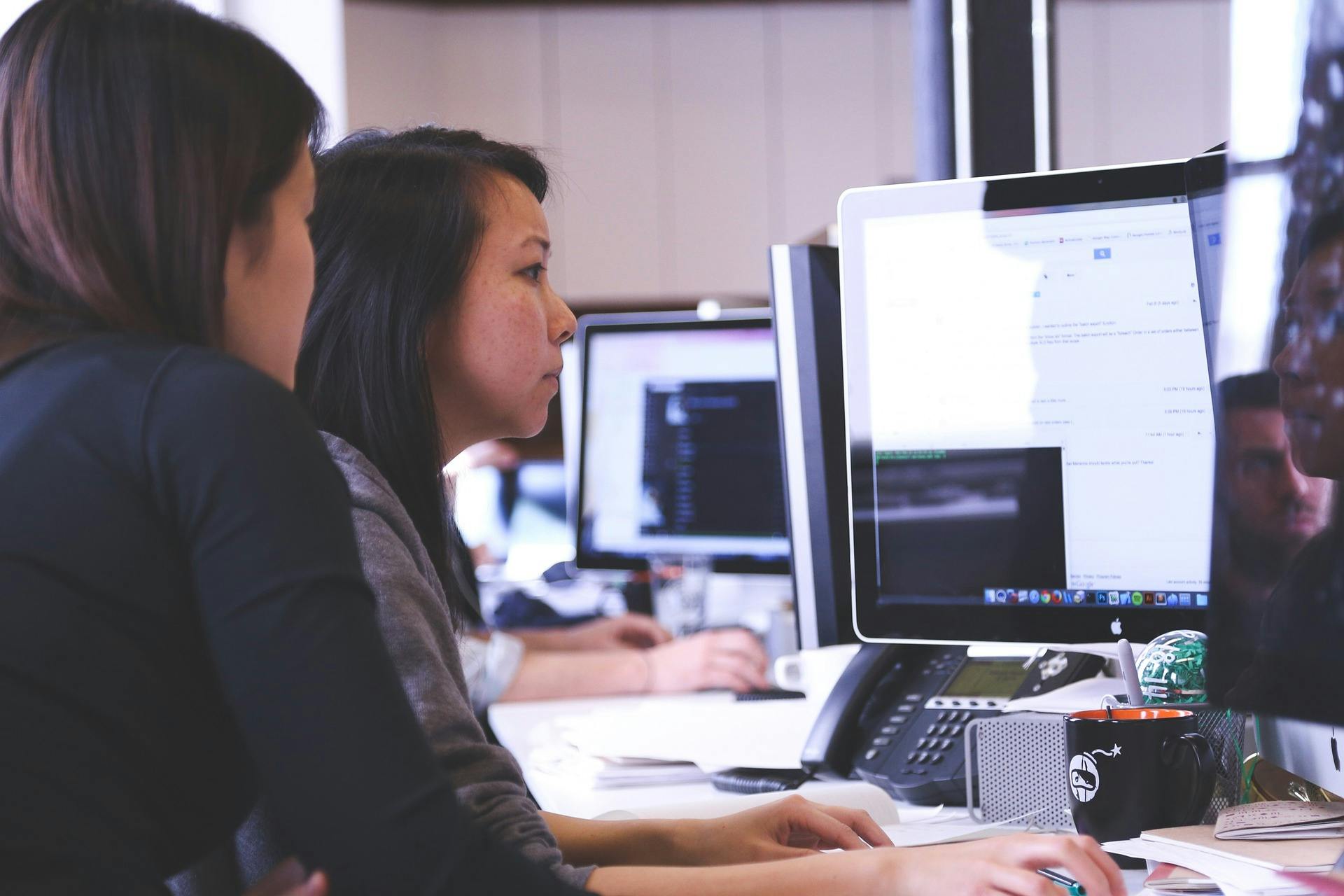 Two women sitting at a desktop computer, learning MongoDB.