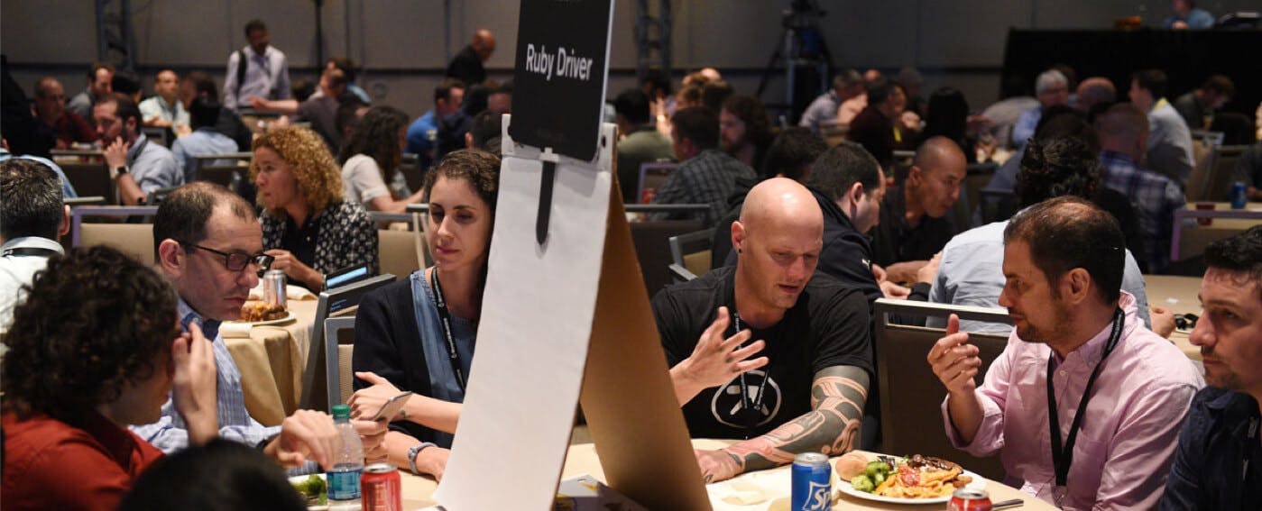 People gather around a table with a sign "Ruby Driver", engaged in discussion.